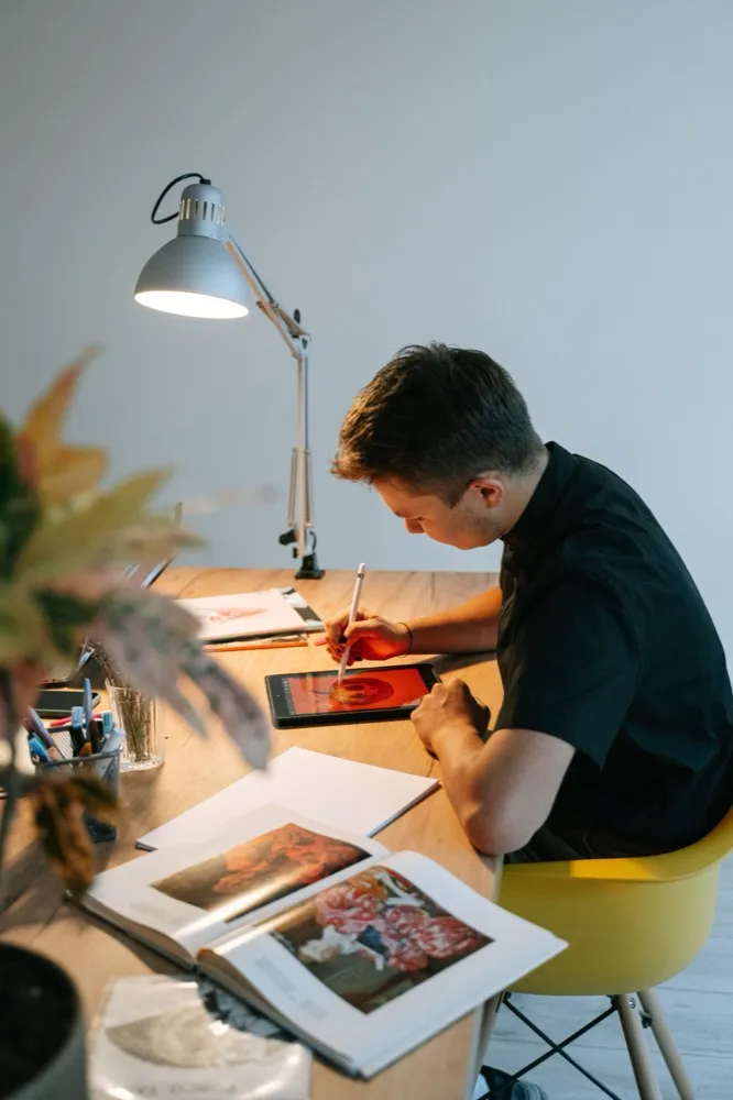 Designer sketching illustration reference at a lamp-lit desk